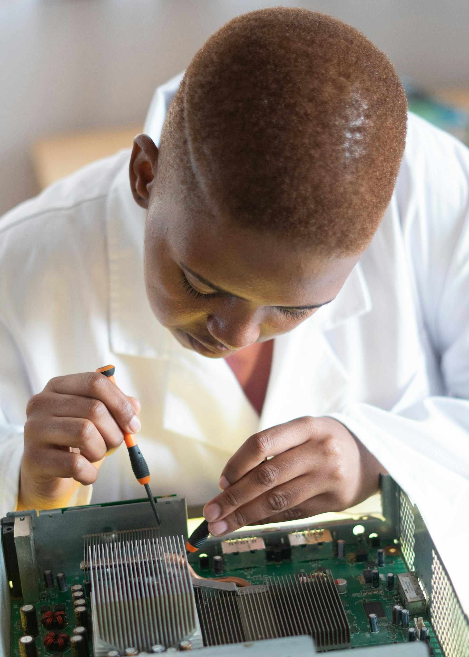 Focused technician in lab coat checking current of electricity with voltmeter while examining condition of graphics card in workshop